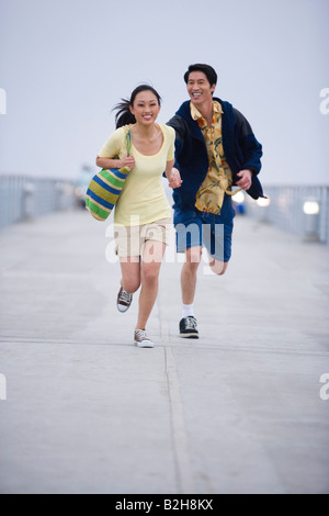 Young couple running on a bridge near the sea and smiling, Huntington Beach, California, USA Stock Photo
