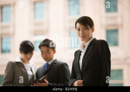 Portrait of a businesswoman with two business executives discussing behind her Stock Photo