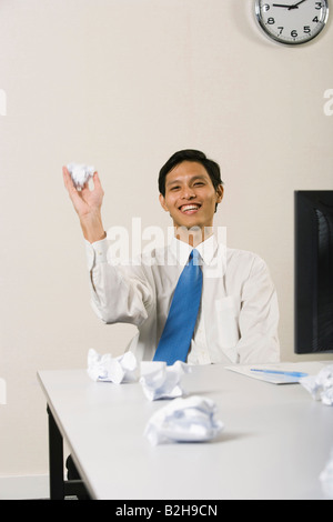 Businessman sitting at a desk and throwing crumpled papers in an office Stock Photo
