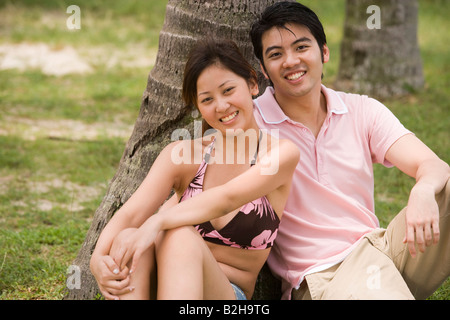 Portrait of a young couple leaning against a tree and smiling Stock Photo