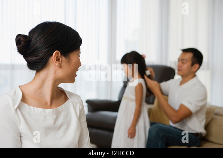 Close-up of a mid adult woman looking at a mid adult man combing his daughter's hair in the background, Singapore Stock Photo