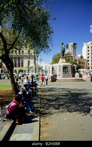 Group of people siting on curb at Church Square near statue of Transvaal Republic President Paul Kruger Pretoria South Africa Stock Photo