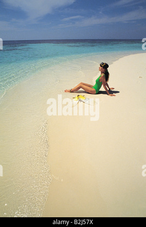 Maldives. Young woman in swimsuit sitting on the beach. Stock Photo
