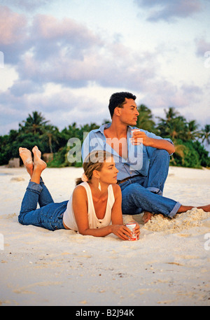 Maldives. Young couple drinking refreshing drinks from cans while relaxing on the tropical beach. Stock Photo