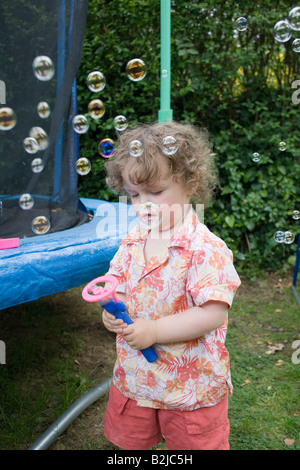Small boy playing with bubble making machine in his back garden. Stock Photo