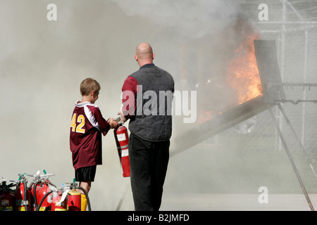 A man demonstrating how to use an extinguisher to a child to put out a fire at a Fire Safety Fair Stock Photo