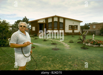 white man white shirt shorts watering garden lawn with hosepipe kleinmond white area south africa 1988 Stock Photo