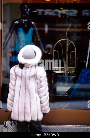 WOMAN WEARING FUR HAT COAT LOOKING AT DRESS DISPLAYED ON MANNEQUIN IN SHOP WINDOW ST MORITZ Stock Photo