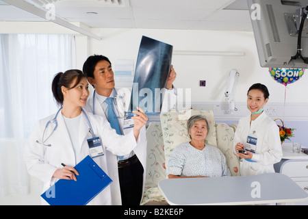 Two doctors examining an X-Ray report with a female nurse and a patient beside them Stock Photo