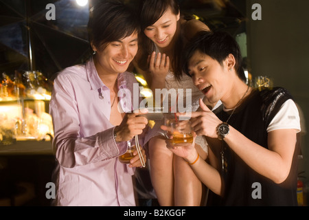 Two young men and a young woman looking at a digital camera and smiling Stock Photo