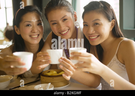 Portrait of three young women having tea in a restaurant and smiling Stock Photo