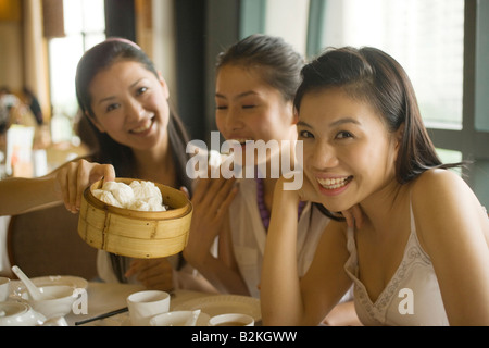 Portrait of a young woman offering Chinese dumpling to her friends in a restaurant and smiling Stock Photo