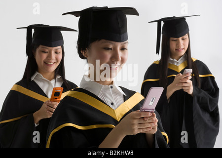 Three female graduate students using mobile phones and smiling Stock Photo