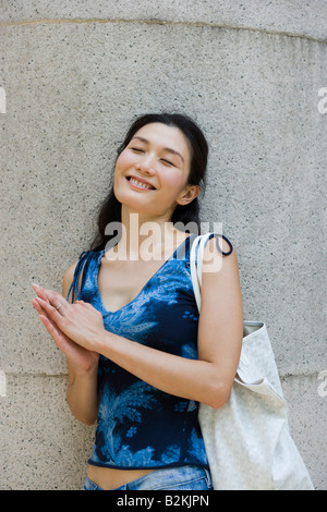 Young woman leaning against a wall and smiling Stock Photo