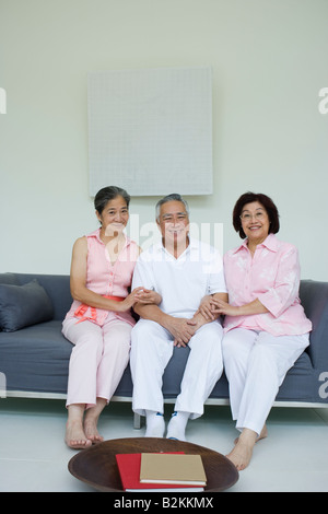 Portrait of a senior man with two senior women sitting on a couch and smiling Stock Photo
