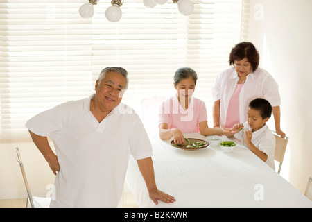 Portrait of a senior man standing with two senior women and a boy podding green peas in the background Stock Photo
