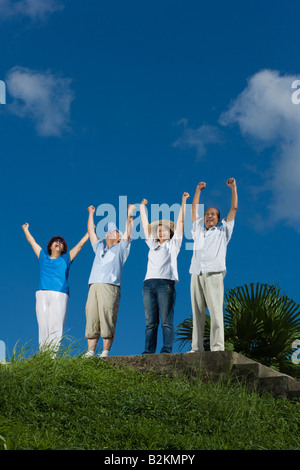 Low angle view of two couples standing with their arms raised in a park Stock Photo