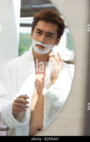 Reflection of a young man applying shaving cream on his face in mirror Stock Photo