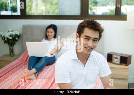 Portrait of a young man smiling with a mid adult woman using a laptop in the background Stock Photo