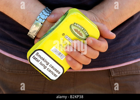 Mans hand holding tabacco tin with health warning Stock Photo
