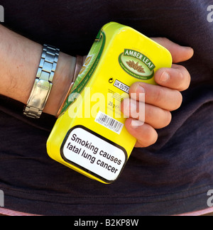 Mans hand holding tabacco tin with health warning Stock Photo