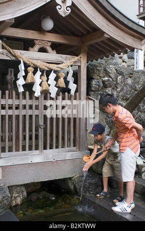 In a Shinto purification ritual a man pours clean water on the hands of a boy standing before a shrine in Gujo Hachiman Stock Photo