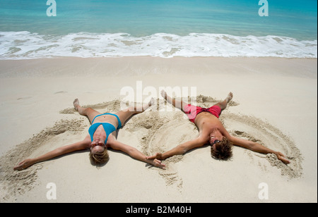 A couple makes snow angels but in warm caribbean sand on secluded 11 Mile Beach in Barbuda Stock Photo