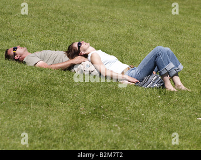 Young couple sun bathing on grass wearing sunglasses in the summer Stock Photo