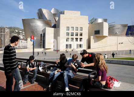 Young people chatting in front of Museo Museum Guggenheim Art Gallery Bilbao Spain One is eating an ice lolly cream Stock Photo