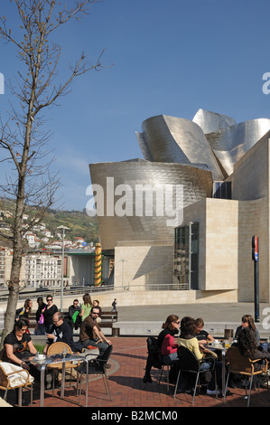 Young people sitting at outdoor café tables in front of Museo Museum Guggenheim Art Gallery Bilbao Spain Stock Photo