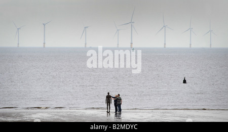 A COUPLE TOUCH ONE OF THE IRON MEN STATUES ON CROSBY BEACH NEAR LIVERPOOL CREATED BY ARTIST ANTONY GORMLEY,UK,ENGLAND. Stock Photo