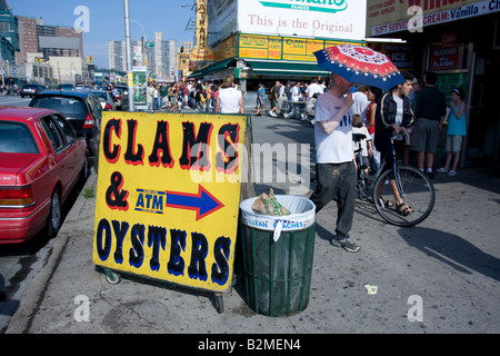 A man carrying an umbrella passes by a 'clams and oysters'  sign at Coney Island, Brooklyn, NY Stock Photo