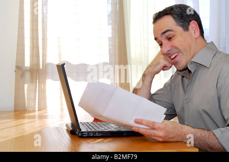 Man sitting at a desk looking at bills and smiling Stock Photo