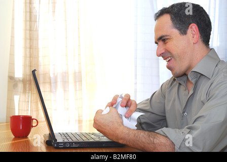 Man sitting at his desk with a laptop crumpling papers Stock Photo