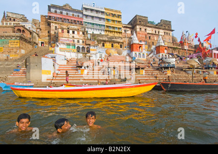 Wide angle view of people on the Ahilyabai Ghat performing their daily ritual with 3 happy young swimmers in the foreground. Stock Photo