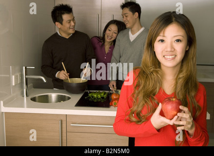Portrait of a young woman holding an apple while friends working in a kitchen Stock Photo
