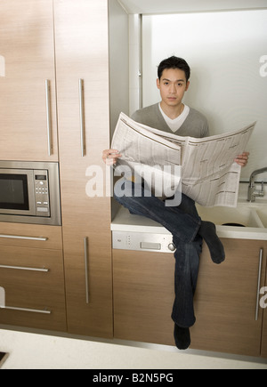 View of a young man reading newspaper in a kitchen Stock Photo