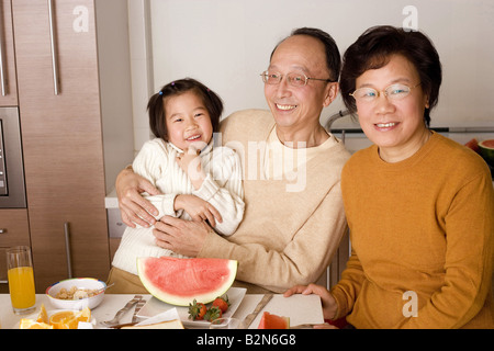 Portrait of a senior couple sitting at a breakfast table with their granddaughter Stock Photo