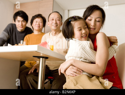 Close-up of a young woman hugging her daughter with her family members at a breakfast table Stock Photo