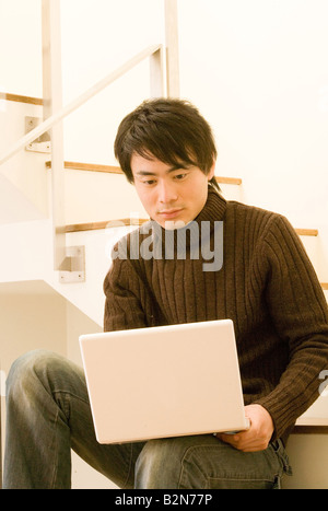 Mid adult man sitting on a staircase and using a laptop Stock Photo