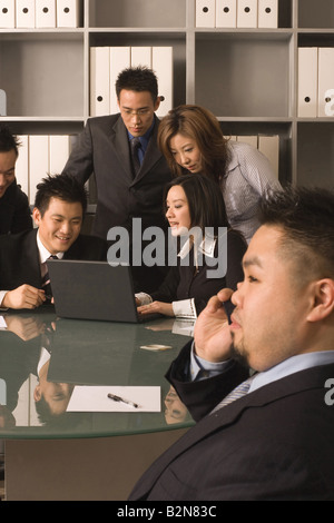 Side profile of a businessman talking on a mobile phone with his colleagues using a laptop Stock Photo