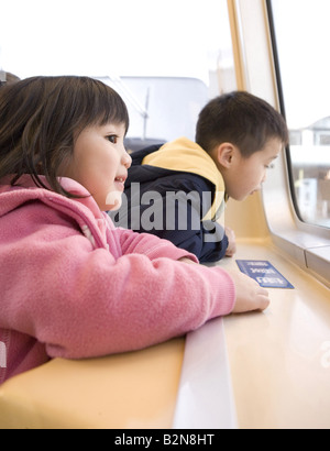 Girl with her brother looking through a window of a train Stock Photo