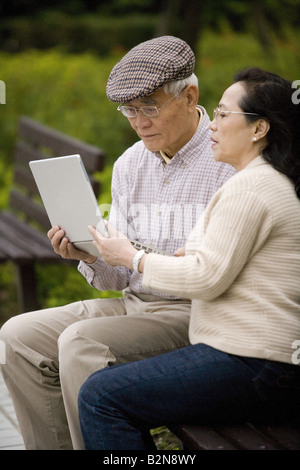 Senior couple sitting on a park bench and using a laptop Stock Photo