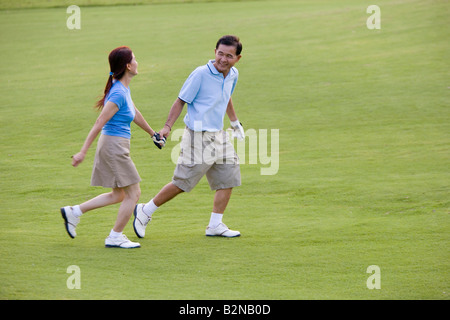 Mature couple holding each other's hands and running in a golf course Stock Photo