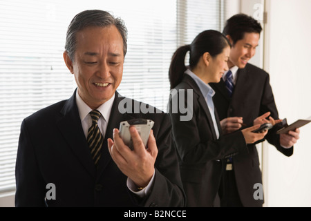 Close-up of a businessman using a mobile phone with two business executives standing behind him Stock Photo