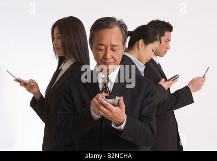 Close-up of a businessman operating a personal data assistant with three business executives standing behind him Stock Photo