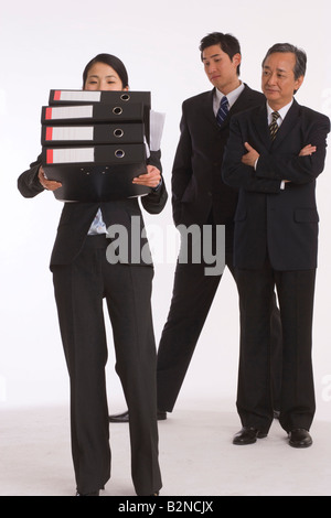 Two businessmen looking at a businesswoman carrying a stack of files Stock Photo