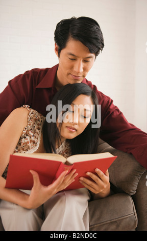 Young woman leaning on a young man's laps and reading a book Stock Photo
