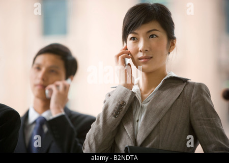 Businesswoman talking on a mobile phone with two business executives standing beside her Stock Photo