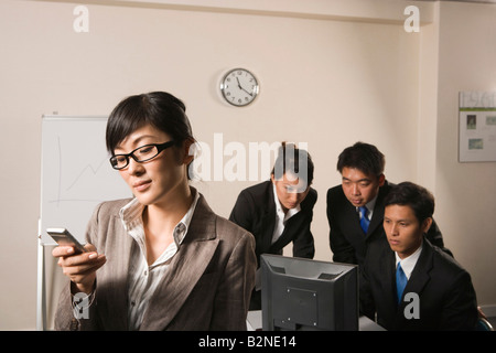 Businesswoman using a mobile phone with three business executives working behind her Stock Photo
